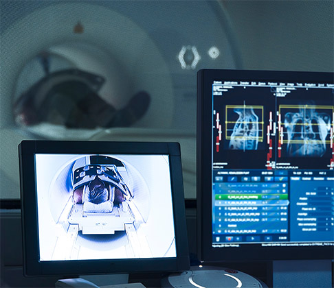 A patient undergoes an MRI in the background while monitors in the foreground show his vital signs and medical imaging.